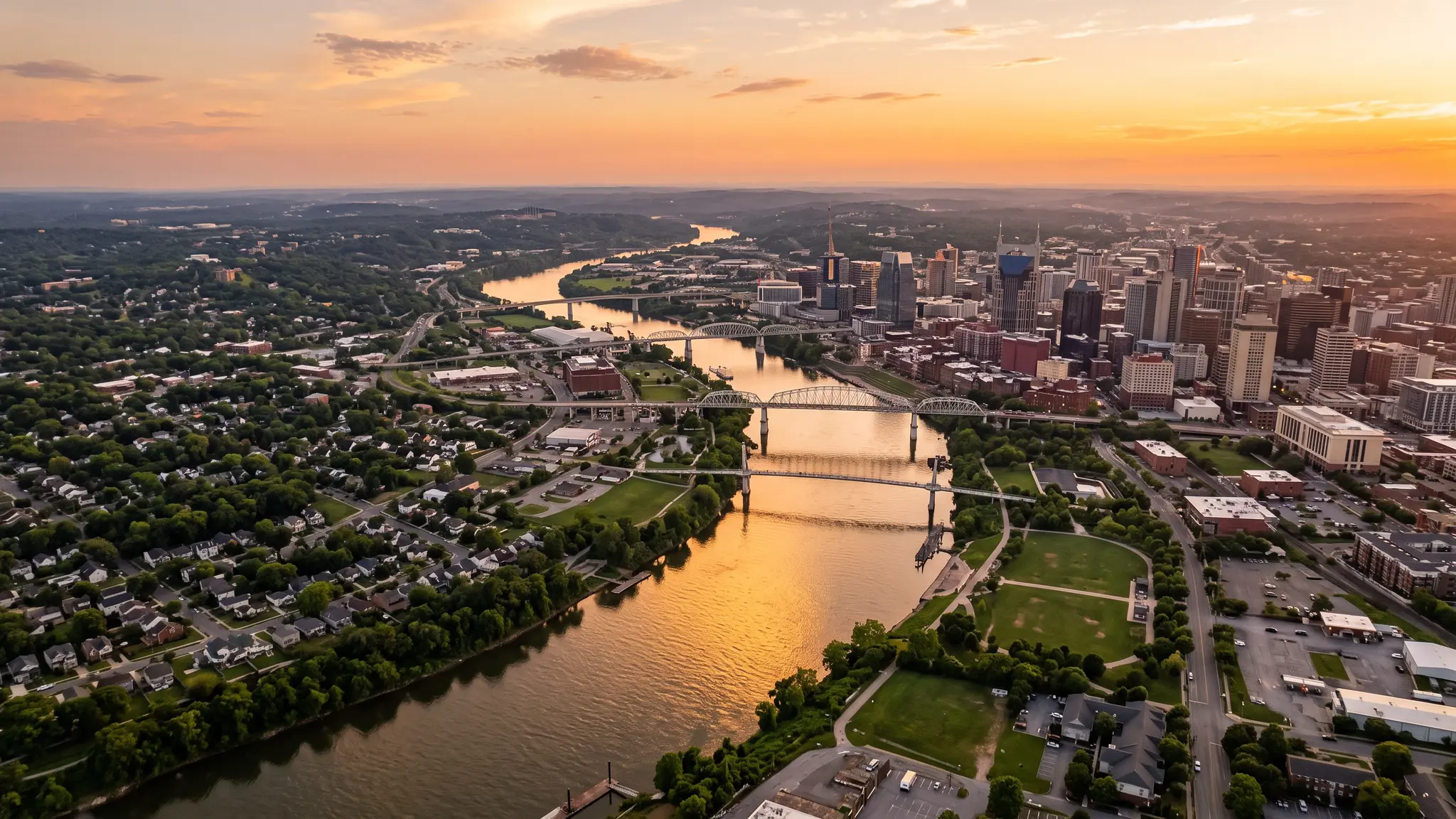 Aerial view of the Cumberland River winding past the Nashville skyline and residential neighborhoods at sunset